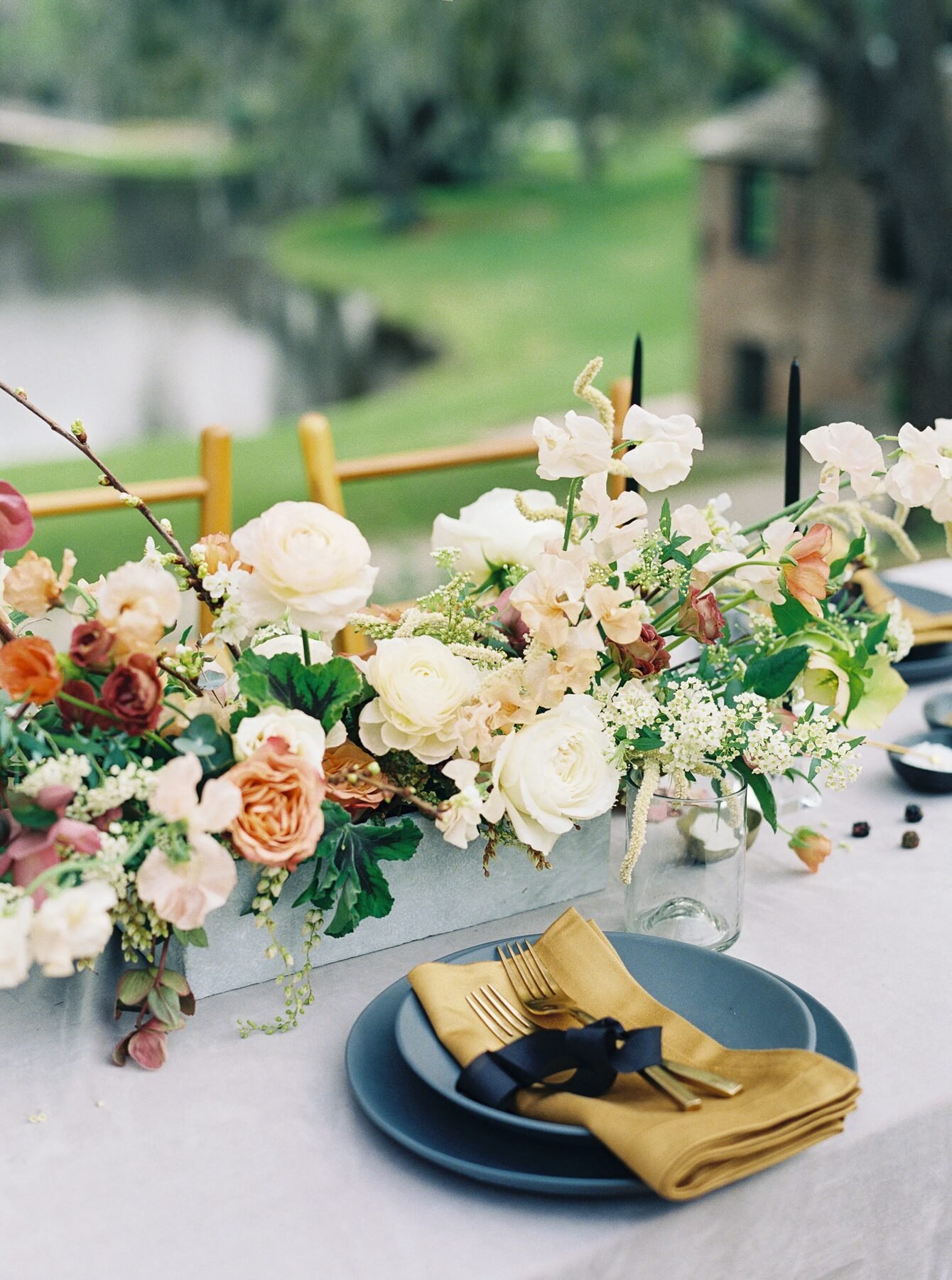 Lowcountry garden tablescape with a long ivory-and-peach centerpiece, slate plates and mustard napkins overlooking a pond