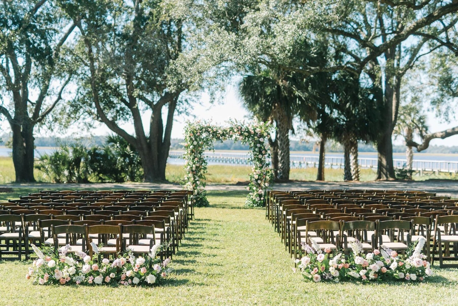 Empty Lowndes Grove ceremony aisle leading to a floral arch under sprawling live oaks with marsh and river view