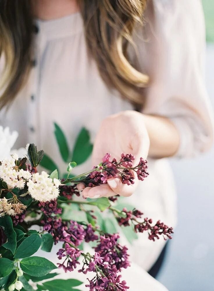 Woman in ivory blouse holding sprigs of lilac and white blooms, soft film portrait of hands working flowers