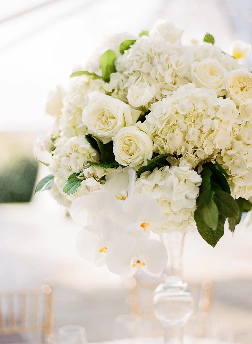 Tall all-white centerpiece of hydrangea, garden roses and cascading orchids in a glass urn