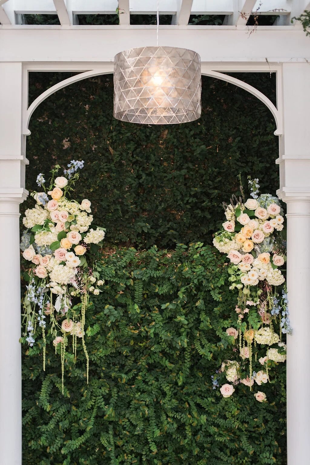 Symmetrical floral install: blush/cream asymmetric arrangements flanking a green fern wall under pendant